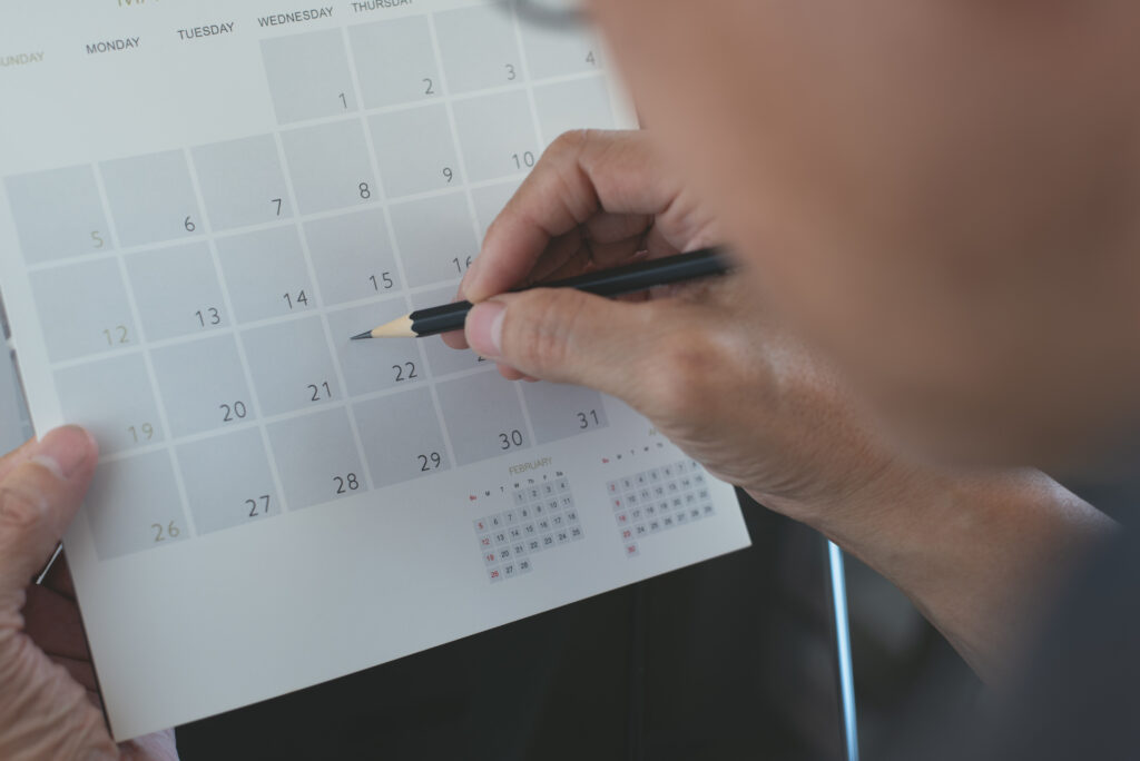 Foto de uma pessoa marcando uma data em um calendário, foco nas mãos, simulando a ideia de organização de despesas fixas.