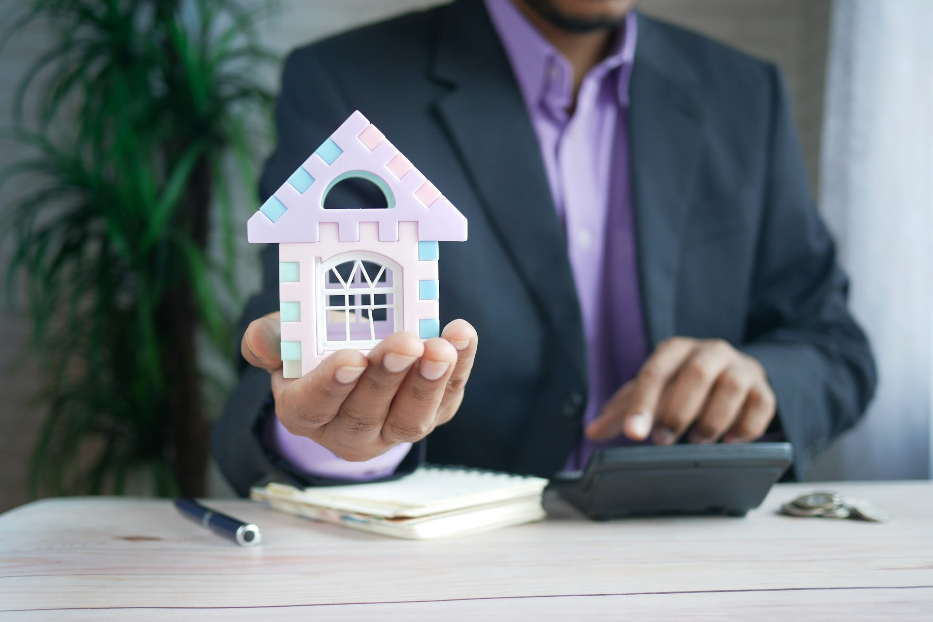Foto de um executivo segurando uma miniatura de casa enquanto faz cálculos, ilustrando a ideia de empréstimo para investir