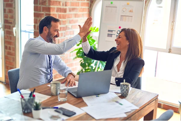 duas pessoas celebrando em uma mesa com folhas de ofício e um notebook